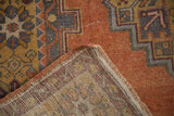 Distressed Oushak rug corner, showing orange pile, stepped geometric design, and muted woven reverse.