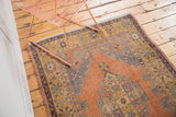 Distressed Oushak rug corner showing aubergine border, apricot field, and stepped rectilinear patterns.