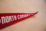 Pointed tip of vintage red felt North Conway pennant, showing white N. H. lettering and aged texture.