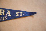 Blue felt pennant tip, showing cream 'ST.' letters with visible pinhole detail.