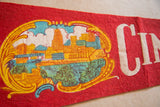 Colorful city skyline graphic and white 'CIN' text on a red felt pennant.