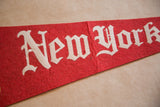 White 'ew York' script on a vintage red felt pennant, showing its texture.