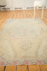Distressed Oushak rug, muted beige rococo patterns, bright pink accents, and light T-stain.