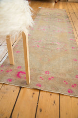 Vibrant pink rose motifs on the distressed beige pile of a Vintage Oushak runner.