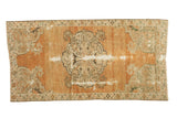 Distressed vintage Oushak rug with faded burnt orange field, scalloped floral medallion, and visible wear.