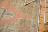 Distressed Oushak rug texture with dusty rose, pale blue, and beige serrated geometric patterns.
