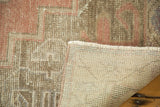 Folded vintage distressed Turkish Oushak rug showing muted pile, hand-knotted backing, and fringe.