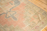 Distressed Oushak rug corner showing muted rose, beige, and faded blue border motifs.