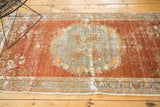 Distressed Oushak runner with muted cinnabar and rococo-influenced floral medallion.
