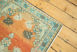 Distressed vintage Oushak rug corner, featuring vibrant burnt orange field and blue geometric border.