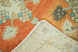 Distressed vintage Oushak rug corner with vibrant orange pile, blue floral motifs, and hand-knotted backing.