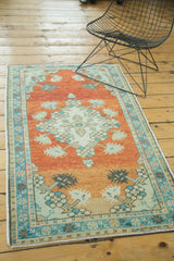Distressed Oushak rug detail with abrash on orange field, blue border, and floral motifs.