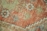 Distressed Oushak rug pile with red, green, and ivory stepped border detail.