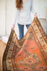 Vintage Malayer rug held, showcasing diamond medallion with rams horn motif and apricot blush field.