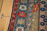 Secured edge of an antique Caucasian rug with vertical geometric patterns in brick red, blue, and camel.