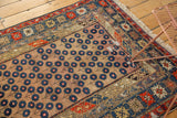 Geometric borders frame a repeating blue blossomed flower motif on this antique Caucasian rug.