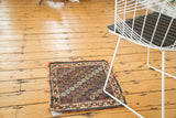 Vintage Afshar rug mat, repeating gul motif in indigo, wine red, and ivory, with frayed edges.