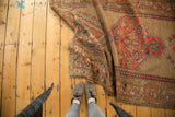 Antique Caucasian rug partially unfurled, revealing asymmetric rectilinear floral medallion.