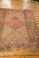 Hard tatter at one end of the antique Caucasian rug, featuring camel, blush, and navy rectilinear patterns.