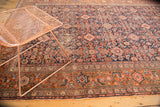 Intricate Herati motifs with diamond panels on navy, bordering a patterned terracotta frame.