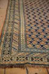 Corner of antique Caucasian rug: navy blue boteh field, multi-layered geometric borders, and fringe.