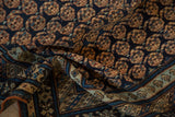 Folded antique Caucasian rug showing intricate navy boteh field and abrashed pale blue border.