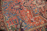 Antique Heriz rug with vivid brick red and blue field, showing speckled floral motifs.
