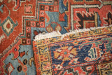 Folded edge of an antique Heriz carpet, revealing foundation and geometric motifs in brick red and blue.
