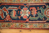 Vivid brick red and navy geometric border on antique Heriz rug, showing knot wear and tatter.