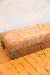 Elongated antique Turkish rug ottoman displaying traditional pink and yellow patterns, brass casters.