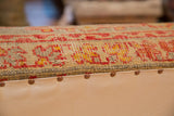 Side detail of extra long ottoman: antique Turkish rug fragment in pink, yellow, aqua; copper studs on canvas.