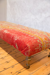 Ottoman side upholstered in distressed antique Turkish rug fragment, red and yellow, with brass leg.