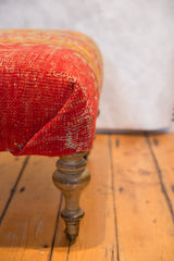 Textured antique Turkish rug fragment ottoman corner with turned wooden leg and brass wheel.