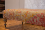 Side view of antique Turkish rug ottoman, highlighting pink and yellow handwoven pattern and leg.