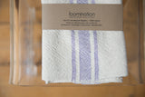 Handwoven Loomination napkin, lavender cream stripes, natural cotton texture, brand label.