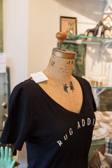 Black v-neck Rug Addict t-shirt with shoulder tag displayed on a vintage dress form.
