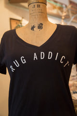 White 'Rug Addict' block letters arched on the chest of a black V-neck t-shirt.