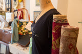 Women's black V-neck t-shirt styled on a dress form beside rolled vintage rugs.