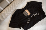 Black Rug Addict v-neck t-shirt with tags, styled next to a rolled herringbone rug.