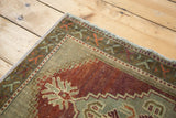 Oushak rug corner, dusty wine field with celadon palmette, stepped zig-zag, and geometric border.