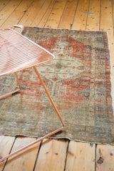 Distressed vintage Oushak rug with faded brick red, ivory patterns, and original selvage.