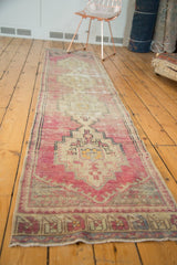 Distressed vintage Turkish Oushak runner with faded mauve, ivory, and charcoal stepped medallions.