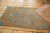 Distressed Oushak fragment reveals oversized floral medallion with even wear and muted beige, green, blue tones.