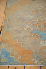Distressed Oushak rug fragment, showing worn beige pile, stepped pale green border, and floral motifs.