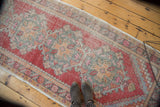 Distressed Oushak runner with cherry red field, seafoam green motifs, and visible worn pile.