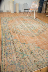 Distressed vintage Oushak rug close-up, worn peach field, mint green, pale blue floral details.