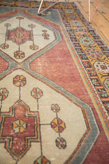 Distressed vintage Oushak runner showcasing ivory pinwheels on wine red with geometric floral border.