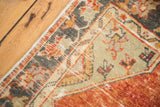 Distressed Oushak rug corner showing worn tangerine field, charcoal and faded red floral border.