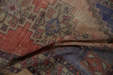 Distressed Oushak rug folds showcasing even wear and time-softened red, blue geometric motifs.