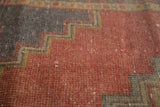 Distressed Oushak rug's faded cinnabar red and dark sand stepped pattern, highlighting worn pile.